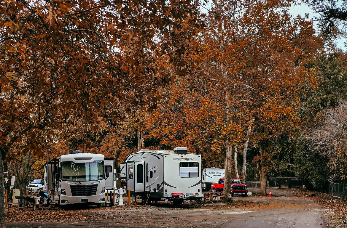Travel trailers parked at a campground beneath a dense canopy of autumn trees